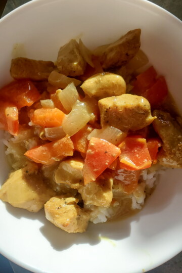 chicken curry recipe completed in a bowl. Chicken, tomatoes, curry powder, onions, and coconut milk.