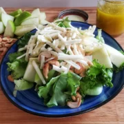 Apple Swiss salad from Cleveland cooking. green leaf salad with shredded Swiss, cashews, and granny Smith apples. a jar of the dressing in the background along with pieces of apples and cashews. receipt by Cleveland cooking