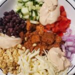 Easy spiced pork recipe by cleveland cooking. burrito bowl with corn, onion, everything sauce, cheese, black beans, cucumber, and red bell pepper