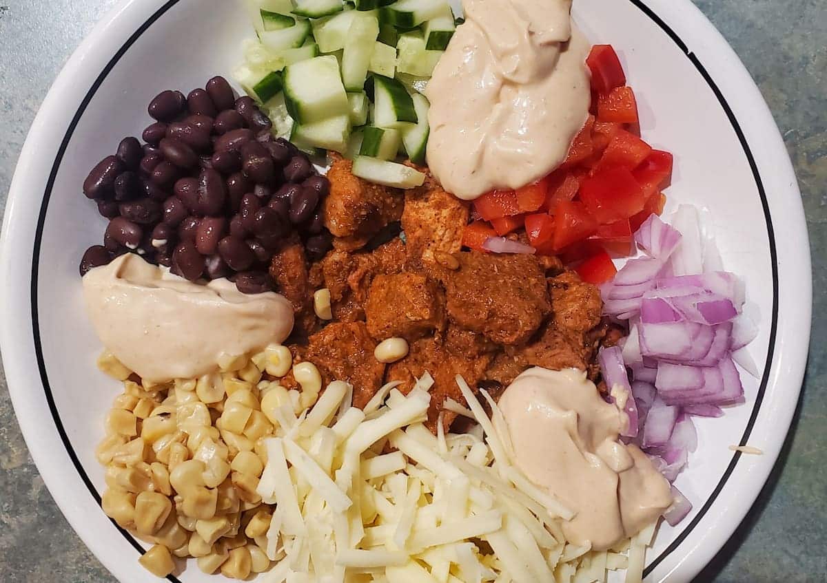 Easy spiced pork recipe by cleveland cooking. burrito bowl with corn, onion, everything sauce, cheese, black beans, cucumber, and red bell pepper