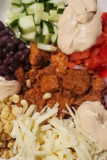 Easy spiced pork recipe by cleveland cooking. burrito bowl with corn, onion, everything sauce, cheese, black beans, cucumber, and red bell pepper
