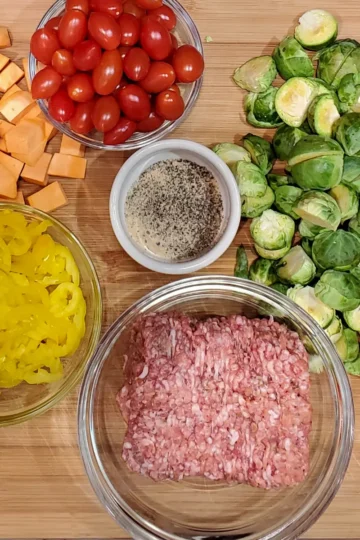 Italian sausage sheet pan recipe from cleveland cooking. All the ingredients are on a large cutting board and are used in the recipe. Italian sausage, olive oil, bell peppers, red onions, sweet potatoes, tomatoes, and banana peppers.
