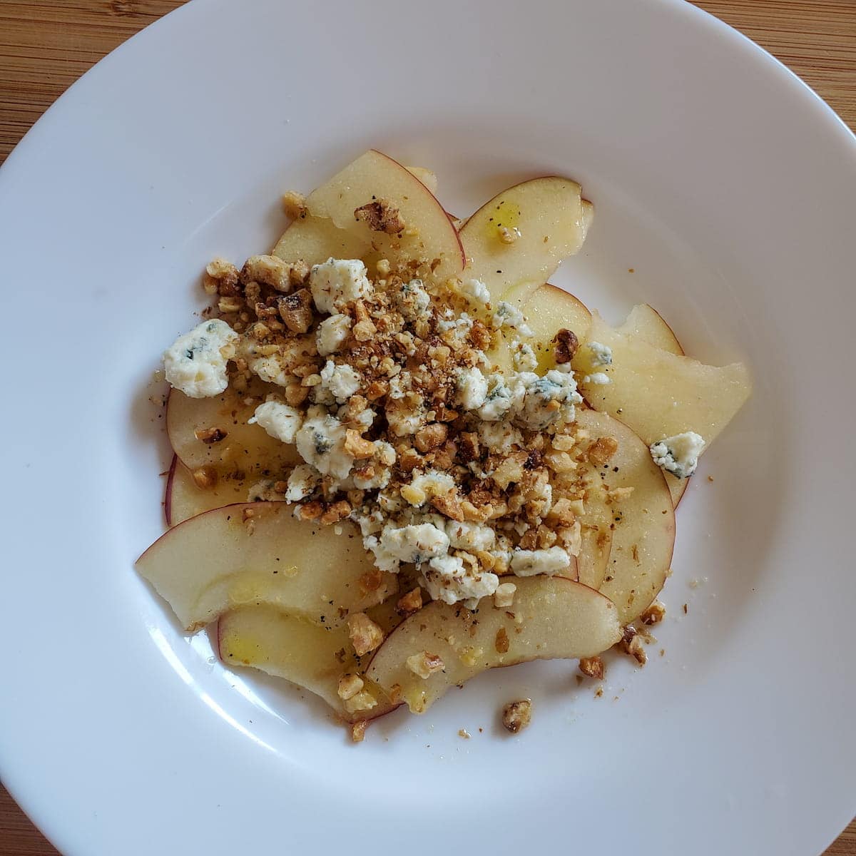 Apple and blue cheese salad with an apple cider vinaigrette. Thinly sliced apples with toasted walnuts and blue cheese.