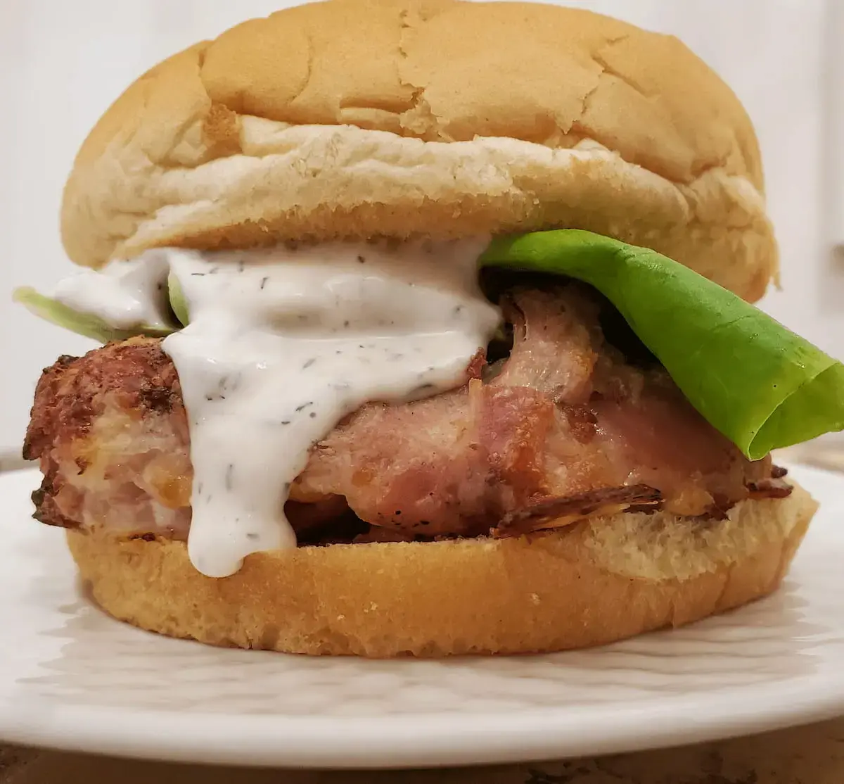 low carb bacon chicken cakes by Cleveland cooking. a low carb bacon chicken cakes on a bun with lettuce and ranch dressing.
