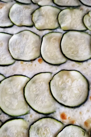 zucchini pizza with garlic cream sauce from Cleveland cooking. sliced zucchini on top of a garlic cream sauce with asiago cheese.