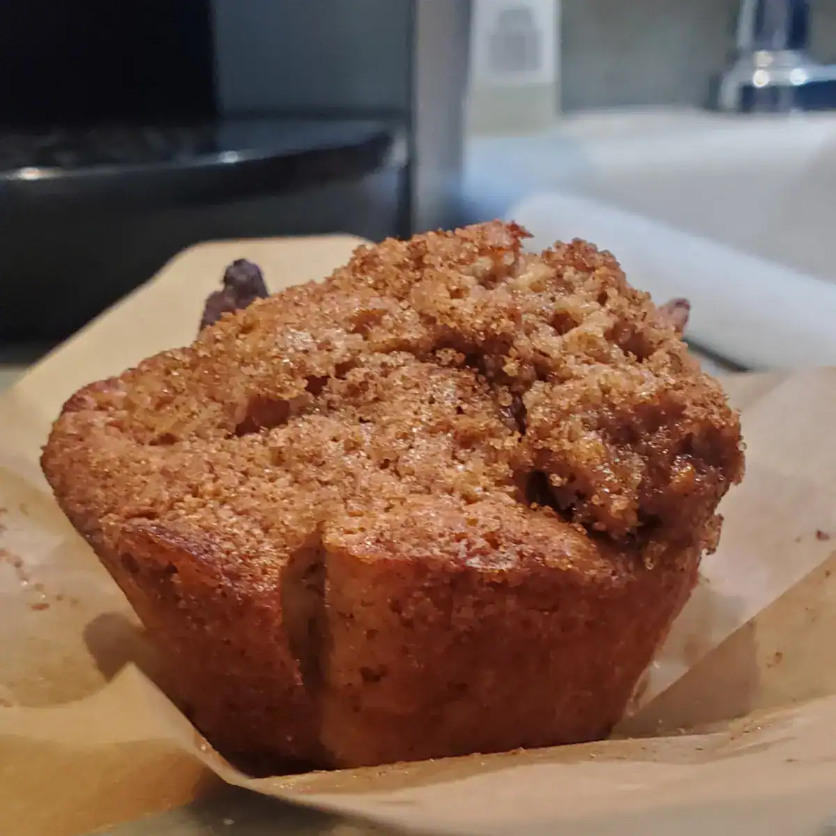 Apple cinnamon muffins separated from it's tulip natural parchment muffin liners. The liner unfolds flat. The muffins shows caramelization of brown and white sugars on the top and the golden brown muffin base. Ceveland cooking.