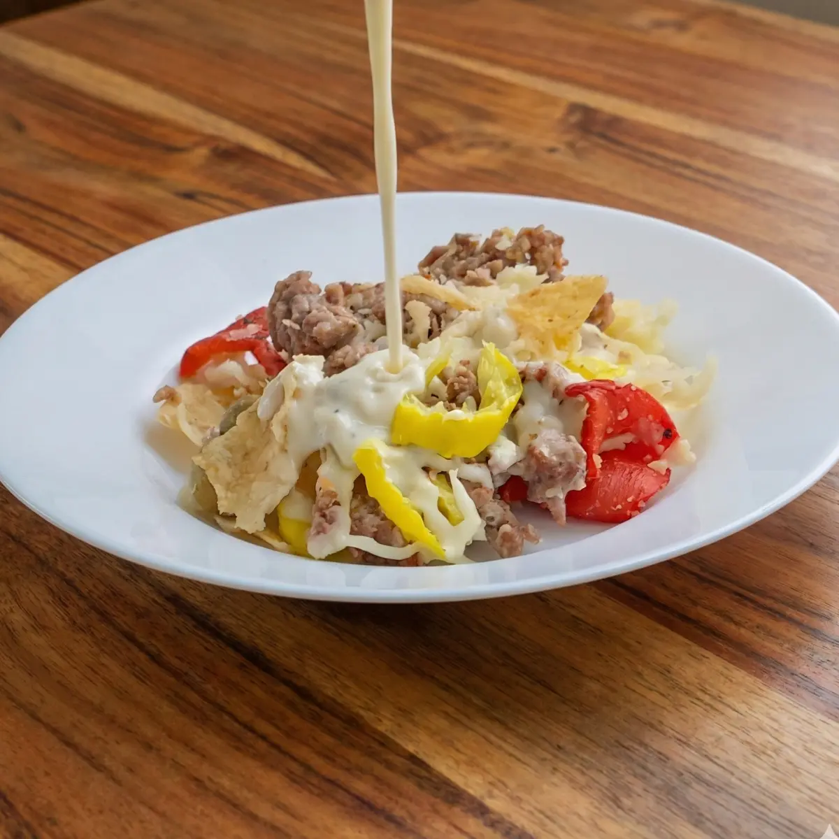 Asiago Cream sauce being poured onto a plate of Italian nachos.