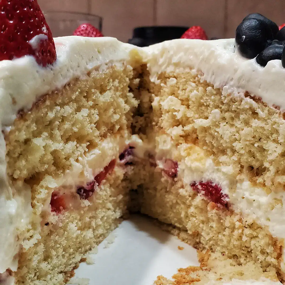 side view of a vanilla cake with strawberries, blueberries, and Chantilly Frosting.