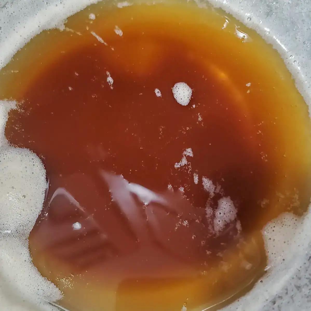 brown butter cooling in a bowl. There is a little bit of white milk solids around the edges.