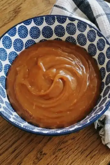 brown butter caramel sauce in a bowl. a blue and white dish towel next to the bowl