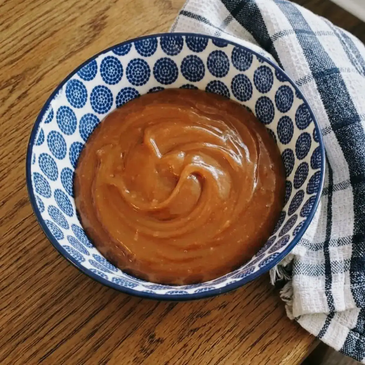 brown butter caramel sauce in a bowl. a blue and white dish towel next to the bowl